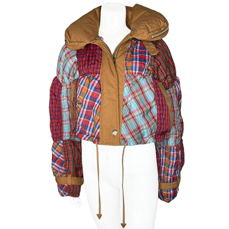 Tsumori Chisato long sleeved patchwork reversible hooded puffer jacket featuring a mix of madras & tartan fabrics with brown leather & canvas accent straps at wrists and pockets. Front zip closure with button, drawstring at waistline, puffy collar zips open to reveal hood. Reversible to all brown with zip-in tartan hood. Made in Japan 